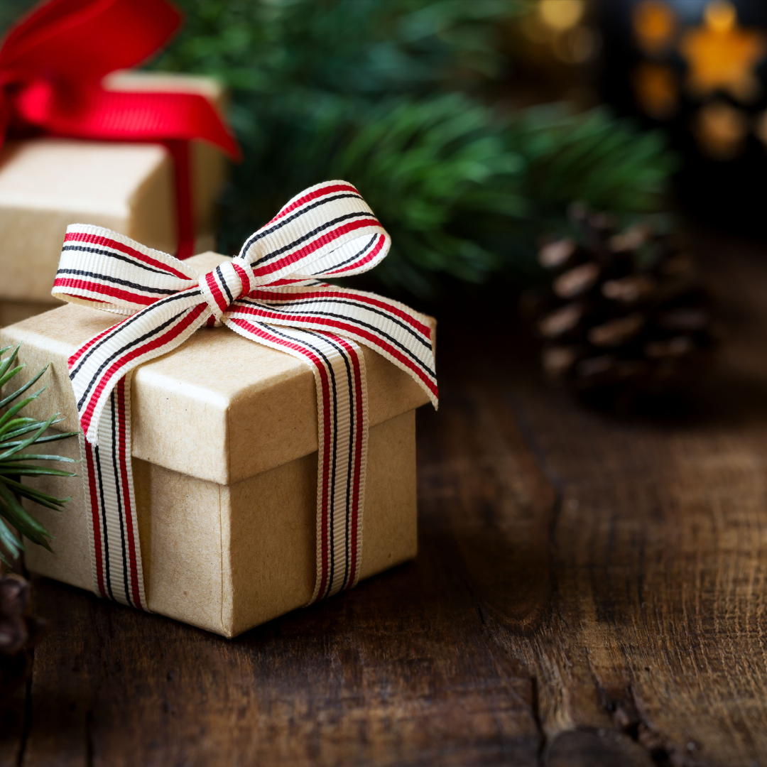 Close-up of a gift box with a striped ribbon, surrounded by pinecones and greenery, perfect for holiday gifting.